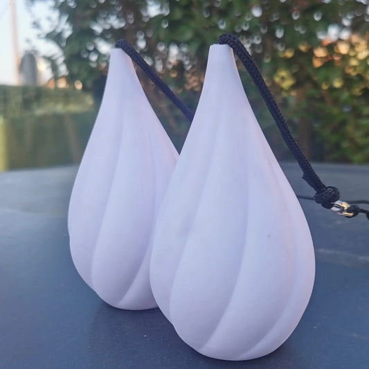 Bolas LED lumineuses Aurora Poi posées sur socle noir, avec un fond végétal.