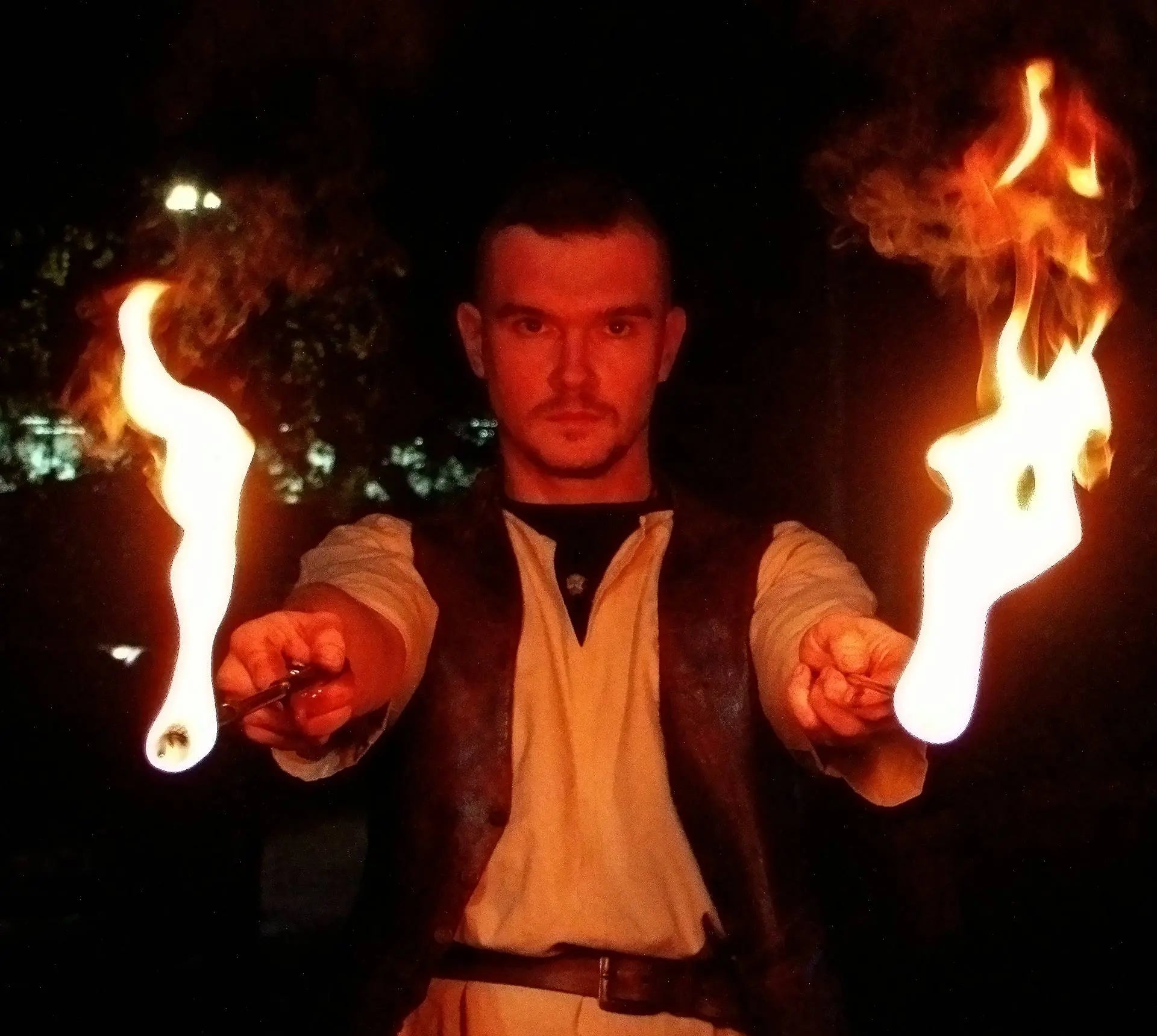 Cracheur de feu à Lyon, portrait de l'artiste avec deux torches enflammées dans la nuit.